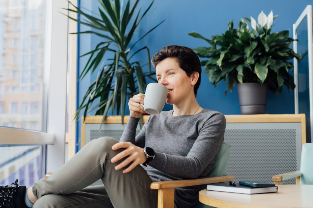 Dreaming Neutral gender middle aged business woman relaxing with coffee cup on the armchair.